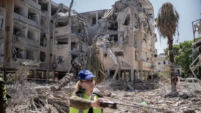 İsrail'in Holon kentinde hasar görmüş evler, önünde bir güvenlik görevlisiyle birlikte