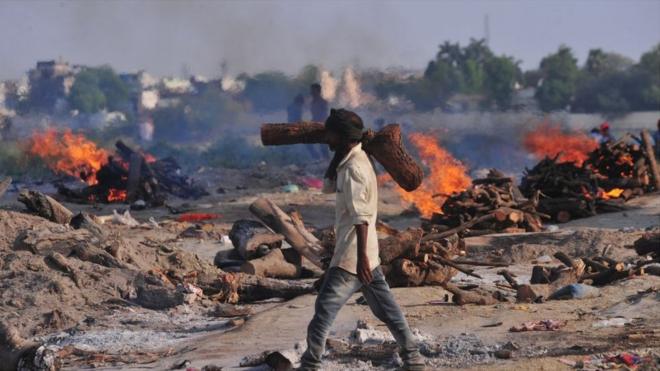A crematorium worker carries wood for the cremation of victims who died from Covid-19 in Allahabad, India