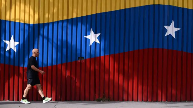 человек идет на фоне венесуэльского флага