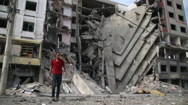 رجل فلسطيني يقف أمام حطام مبنى دمره القصف الإسرائيلي على غزة