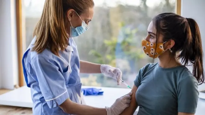 Healthcare worker administers dose of vaccine, as syringe inserted into arm of a young girl,