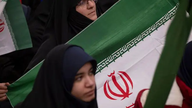 दो बुर्क़ा पहनी ईरानी महिलाएं, 1 फरवरी, 2026 को तेहरान, ईरान के दक्षिण में बेहेश्त-ए ज़हरा कब्रिस्तान में आयतुल्लाह खोमेनी के मकबरे पर ईरान की इस्लामी क्रांति की जीत की 47वीं वर्षगांठ के अवसर पर आयोजित समारोह के दौरान एक राष्ट्रीय ध्वज के पास बैठी हैं