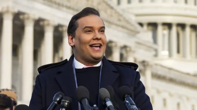 George Santos sorrindo ao falar diante de vários microfones em frente ao Capitólio americano