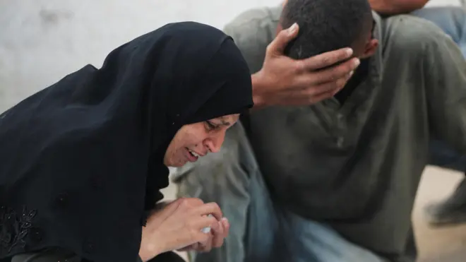 رجل وامرأة فلسطينيان يبكيان على أحد أفراد أسرتهما الذي قتل في استهداف إسرائيلي لتجمعات مواطنين حاولوا الحصول على مساعدات إنسانية