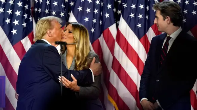 Republican presidential nominee former President Donald Trump, left, kisses Melania Trump as their son Barron Trump looks on at an election night watch party, Wednesday, Nov. 6, 2024, in West Palm Beach, Fla. 