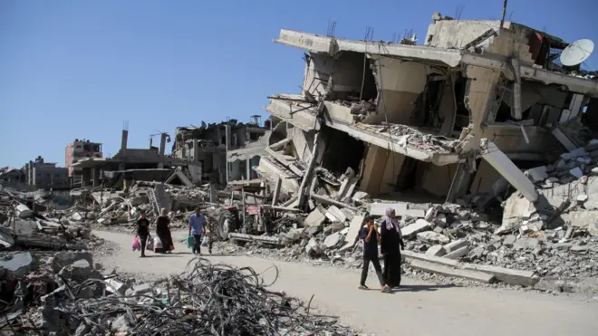 فلسطينيون يسيرون بين أنقاض المباني المتضررة التي دمرت خلال الهجوم العسكري الإسرائيلي، وسط الصراع المستمر بين إسرائيل وحماس، في بيت لاهيا في شمال قطاع غزة.
