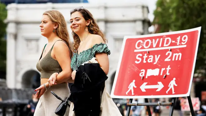 Two women walk past a Covid-19 warning sign in London
