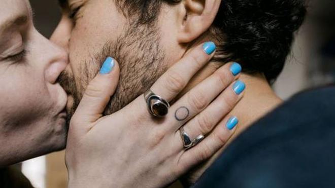 Foto colorida mostra um homem e um mulher brancos se beijando. Ele tem barba e cabelos pretos e ela segura o rosto dele com as mãos com unhas pintadasjogo de máquina caça níquel de moedaazul