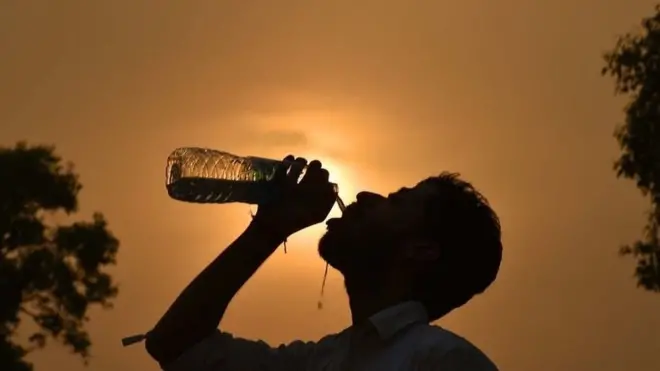 Um homem bebe águasite lampions betuma garrafa com o sol ao fundo