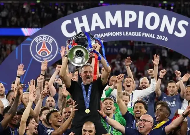 Umutoza Luis Enrique wa Paris Saint-Germain azamuye igikombe cya Champions League ikipe ye yegukanye mu 2026, akikijwe n'abakinyi n'abandi bakozi b'iyo kipe bigaragara ko bishimye. 
