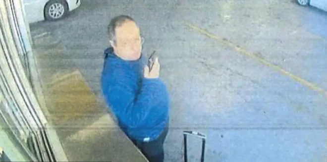 Mavi üst giymiş gözlüklü bir adamın güvenlik kamerası görüntüsüne bakıyoruz. Elinde bir telefona sesli mesaj bırakıyor gibi görünüyor.