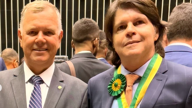 Imagem mostra Lucio Mosquini, à esquerda, de terno cinza, ao lado de Sergio Teixeira, de terno azul marinho, usando uma medalha comemorativa, dentro do Parlamento brasileiro