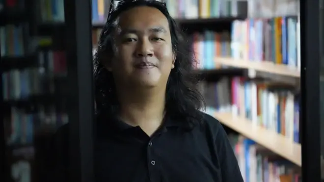 Wakil Koordinator KontraS, Andrie Yunus dengan rambut terurai sebahu sedang menatap kamera sambil tersenyum dengan baju kerah berwarna hitam.