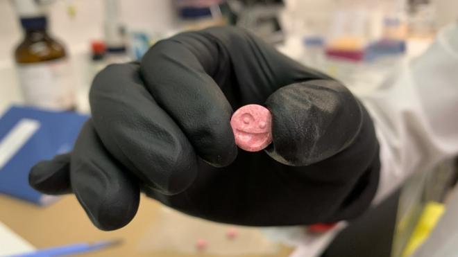 Luva mostra um comprimido, em ambiente de laboratório