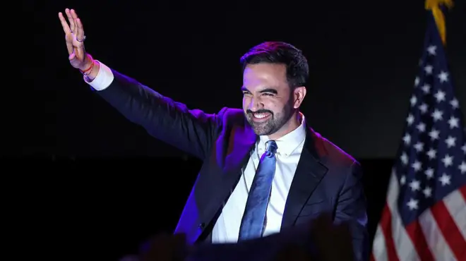 Zohran Mamdani yambaye ikote ry'umukara na karuvati n'ishati y'umweru agaragaza ibyishimo ubwo yizihizaga intsinzi mu birori byo mu ijoro ry'amatora, muri Brooklyn Paramount Theater i Brooklyn, muri New York, muri Amerika.