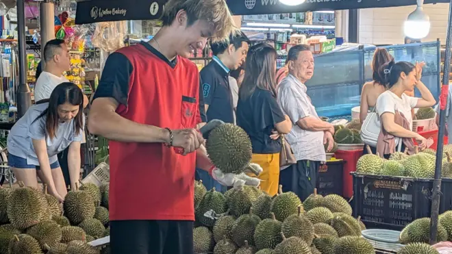 新加坡一位水果攤販正在攤位上開榴槤。