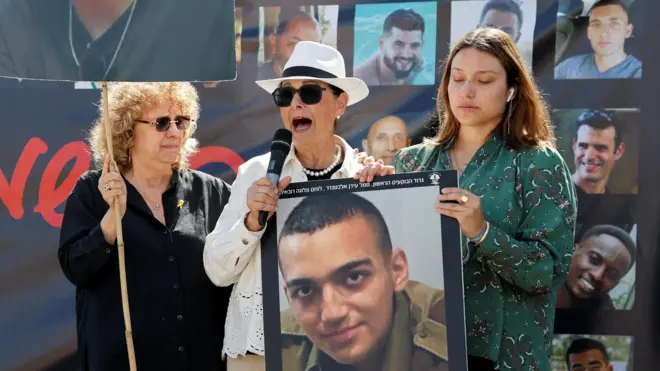  جدة الرهينة عيدان ألكسندر، تتحدث وهي تحمل صورة عيدان، بينما يقف أفراد الأسرة حولها