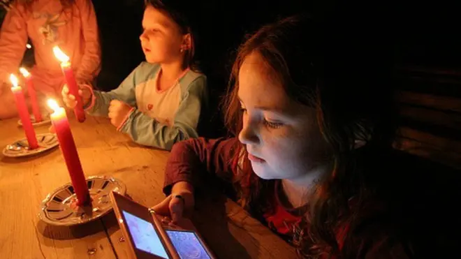 కొవ్వొత్తుల వెలుగులో ఫోన్ వీక్షిస్తున్న చిన్నారులు