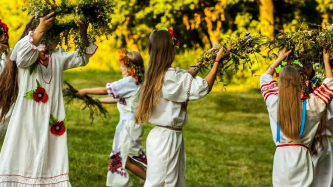 Дівчата-підлітки у національних костюмах тримають сплетені вінки, водять хоровод