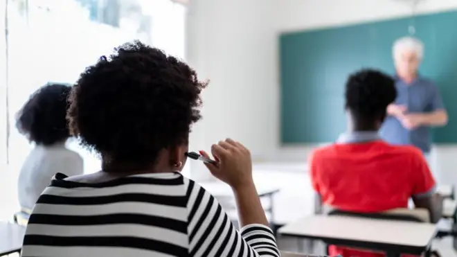 Alunos adolescentescostas, sentados, olhando para professorpé