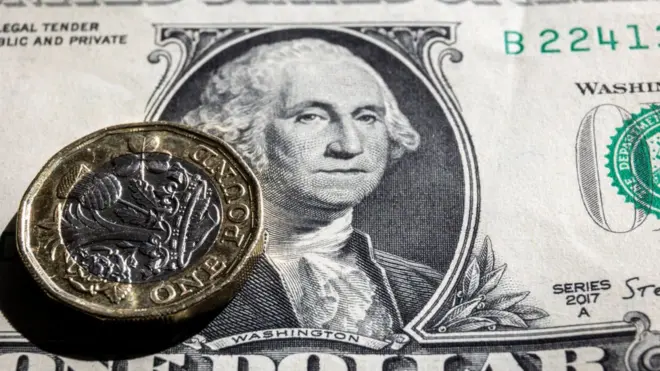 Pound coin on dollar bill.