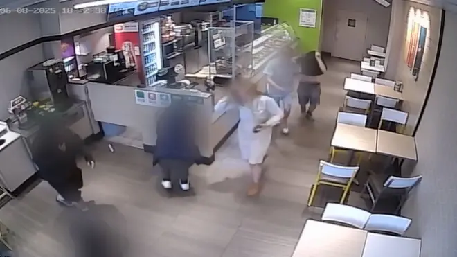 A group of teenagers, blurred, run amok in a shop as they carry out antisocial behaviour, as seen from a CCTV camera at a high angle.