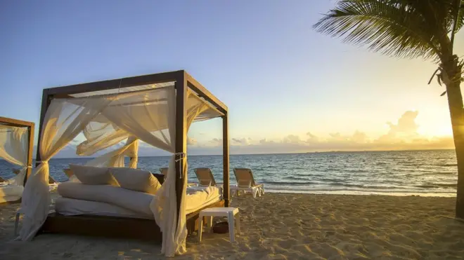 A four poster bed on a tropical beach, at sunset