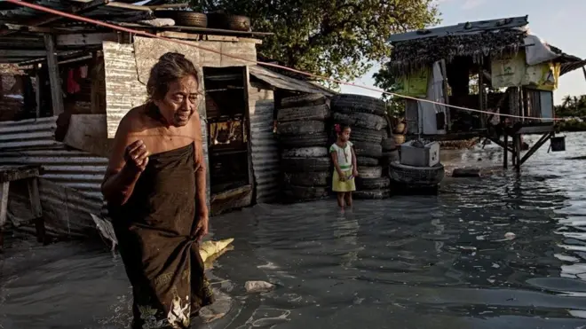 Seorang perempuan berjalan di jalanan yang banjir di Kiritimati.