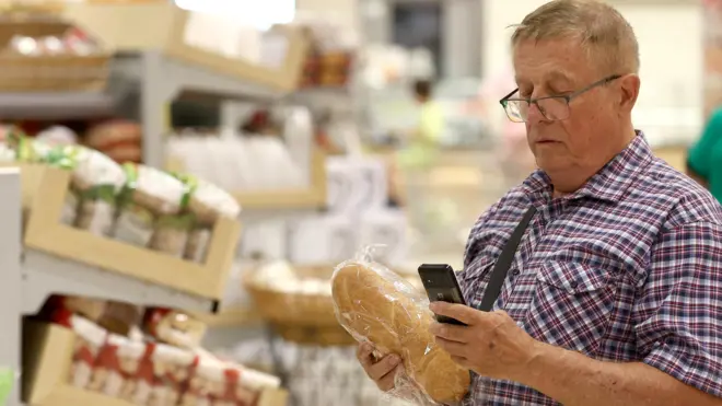 мужчина в супермаркете держит в руке батон хлеба