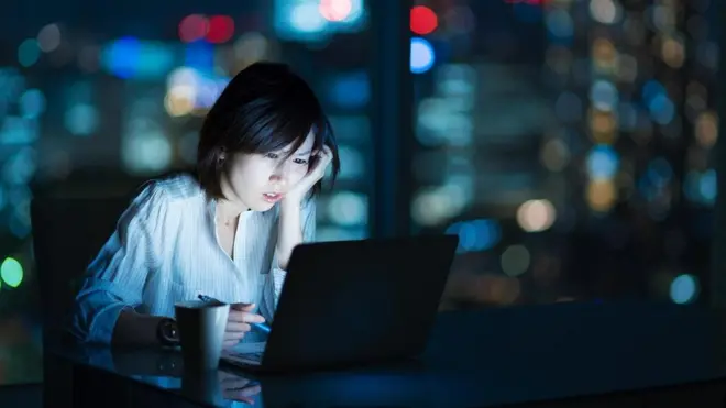 موظفة تعمل ليلا على جهاز كمبيوتر محمول