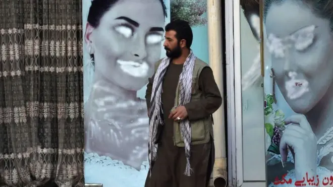 A man stands next to a beauty salon with images of women defaced using spray paint at Shahr-e Naw neighbourhood in Kabul on December 9, 2021.
