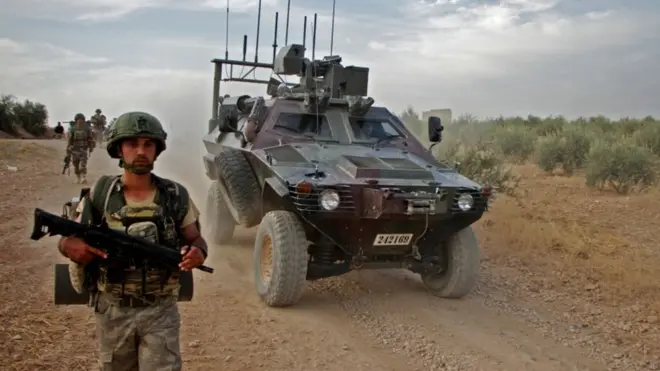 جندي تركي يسير بالقرب من مركبة مدرعة على مشارف منبج شمال سوريا