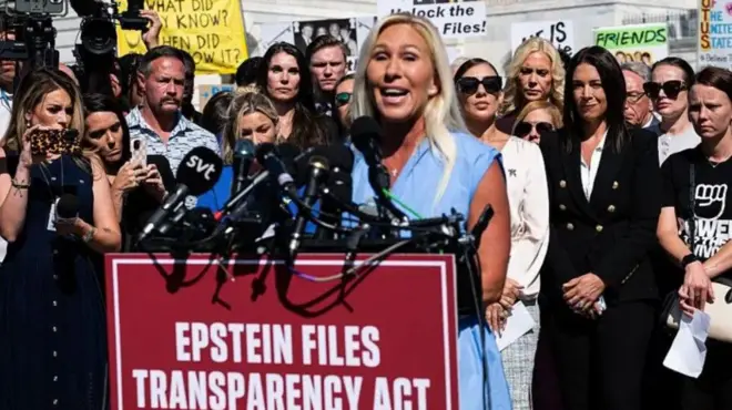 Марджори Тейлор Грин выступает перед стендом с микрофонами на фоне группы людей, требующих раскрытия файлов Эпштейна