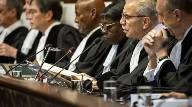 Un banc de juges de la CIJ en robe noire et blanche avec leur mircophone devant eux.