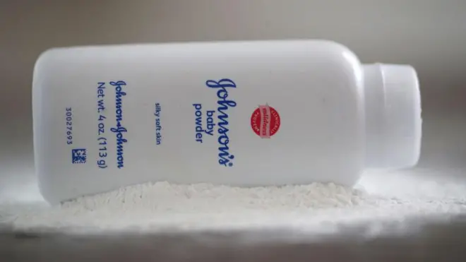 Fotoğraf illüstrasyonunda, Johnson & Johnson marka bir bebek pudrası şişesi, beyaz bebek pudrasının üzerine yan yatırılmış halde görülüyor.