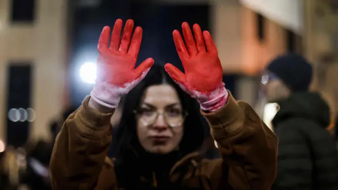 Seorang perempuan mengenakan sarung tangan dengan darah palsu dalam aksi unjuk rasa menentang korupsi dan kelalaian pemerintah yang dituding sebagai penyebab kematian para korban dalam bencana stasiun kereta api Novi Sad pada bulan November, di Beograd, Serbia, 22 Desember 2024.