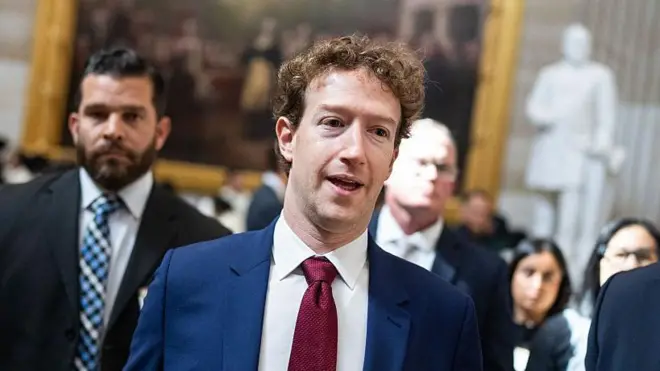 Mark Zuckerberg, vestindo um terno azul e gravata vermelha, caminhando pelo Capitólio.