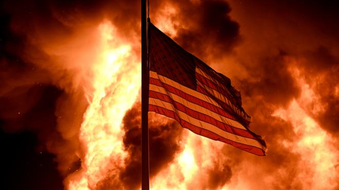 美国威斯康辛州基诺沙市社区矫正大楼前一面美国国旗在示威者纵火点燃的火堆前飘扬（24/8/2020）