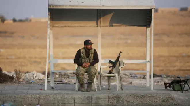 A turkish-backed Syrian fighter sits on the side of the street in the town of Ayn al-Arus