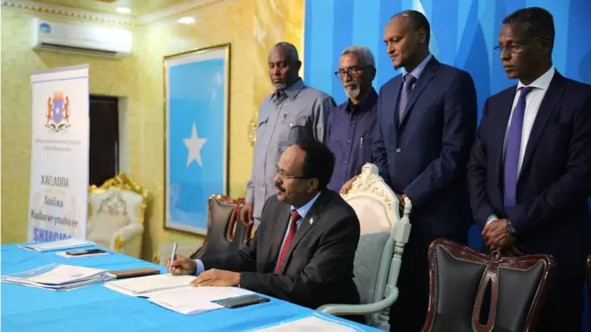 Madaxweyne Maxamed Cabdullaahi Farmaajo oo saxiixay sharciga isgaarsiinta qaranka, waxaa gadaashiisa taagan guddoonka labada aqal iyo xubno ka tirsan xukuumadda