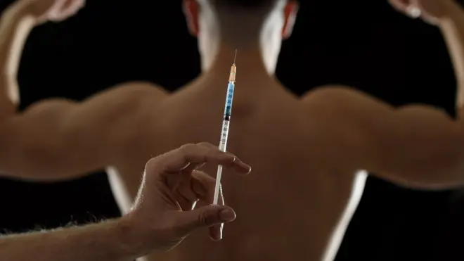 Man holding syringe behind blurred man flexing muscles