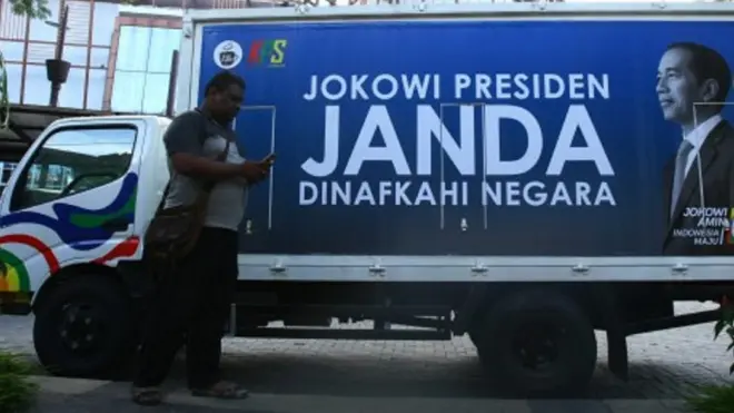 Warga melintas di samping mobil box yang menjadi media alat peraga kampanye (APK) bergambar calon presiden petahana Joko Widodo yang terparkir di sebuah pusat perbelanjaan di kawasan Serpong, Tangerang, Banten, Minggu (17/2/2019).