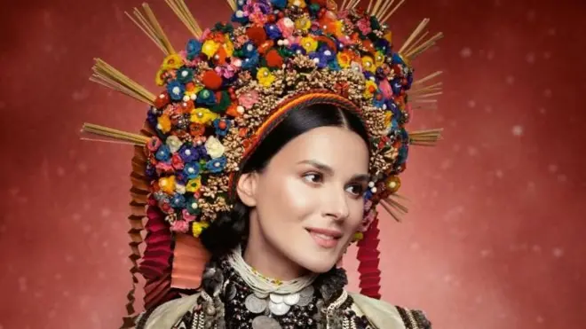 На фото - Маша Єфросиніна. Вбрання: сорочка з домотканого полотна, вишита вовняними нитками; поясне вбрання - опинка, кожушок "з раками", оздоблений вовняними шнурами, прикраси зі срібних монет, перли. Весільний вінок із дутих скляних намистин, квітів зі стружки та стрічок. Село Корнич, Покуття, початок ХХ століття