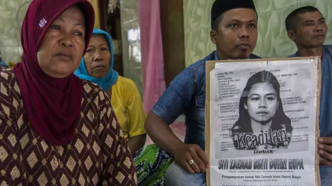 Family members of beheaded Indonesian maid Siti Zainab hold up a poster (R) bearing her portrait at their family home in Bangkalan in East Java province on 15 April 2015