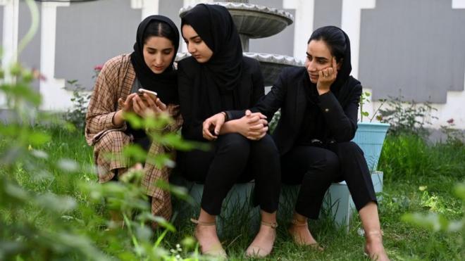 In this photograph taken on May 28, 2022, an Afghan female presenter with news network 1TV, Lima Spesaly (R) sits in a yard with her colleagues Masheed Barzz (C) and Shagofa Salimi at the 1TV channel station in Kabul.