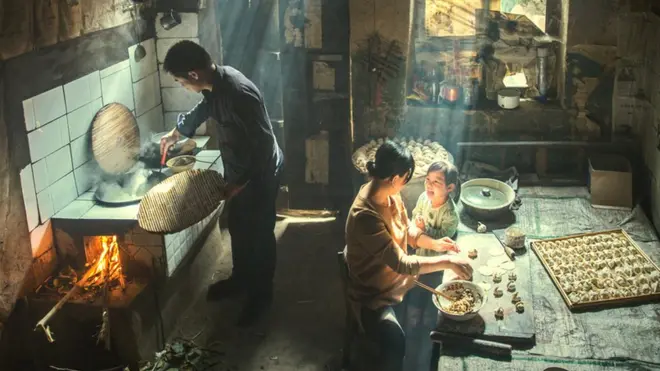 Family preparing food indoors, with rays of sunlight shining through the windows