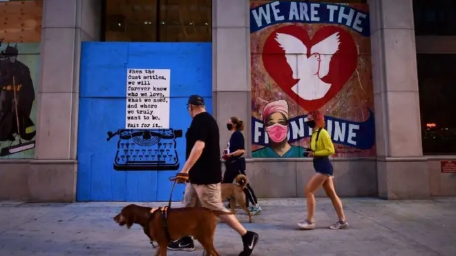 Tiga orang warga AS melintas di depan mural bertema virus corona di sudut kota Los Angeles, 28 April 2020.