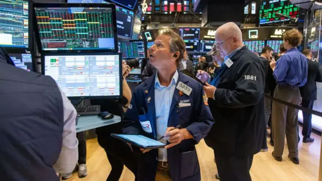 紐約證券交易所內,一名手持筆和筆記本的男子正抬頭看著顯示價格的電腦螢幕。(06/11/2024)