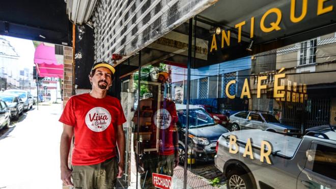 Guto Lima em frente a fachada de sua loja, com vidro escrito 'Antique Café'