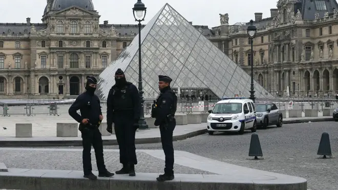 Tres policías parados a las afueras del Louvre.